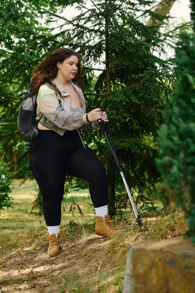 stock image A confident plus size woman takes a moment to hike amidst the greenery of a tranquil forest.