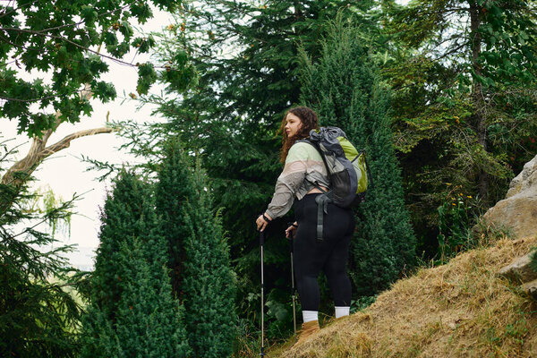 A confident plus size woman enjoys her hike amidst tall greenery and vibrant nature.