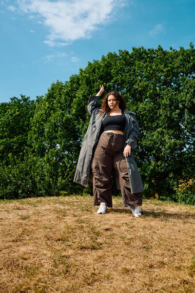 A confident plus size woman strikes a pose in a sunny field, enjoying natures beauty.