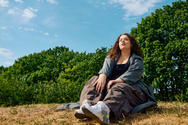 Радостный плюс размер женщина расслабляется на вершине холма под ясным голубым небом в ярком поле.