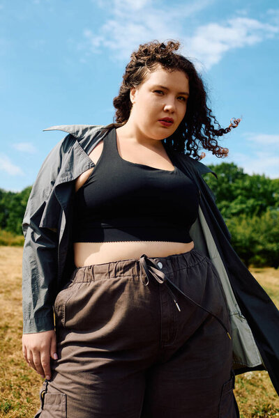 A stylish plus size woman stands proudly in a beautiful field, basking in the sunlight.