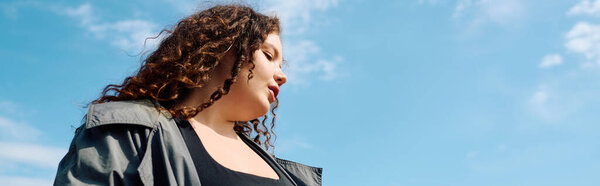 Уверенная в своих размерах женщина стоит посреди яркого поля под ярко-голубым небом, излучая радость.