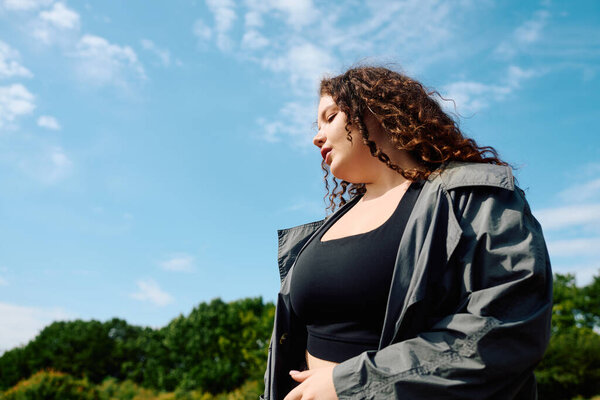 A confident woman revels in the warmth of a sunny day amid lush greenery, celebrating her beauty.