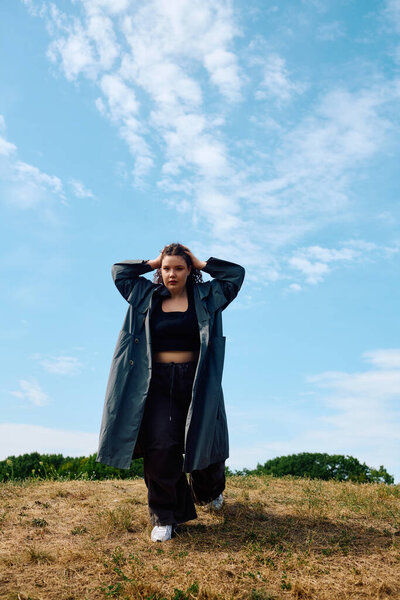 A confident plus size woman poses gracefully in a lush green field, basking in the sunlight.