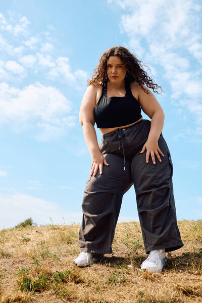 A plus size woman poses gracefully in a sunlit field, embracing nature beauty.