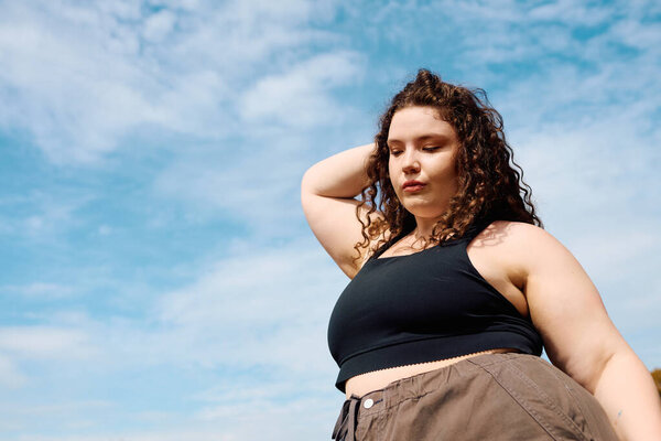 Уверенная в своих размерах женщина грациозно стоит в пышном открытом поле, наслаждаясь солнечным светом.