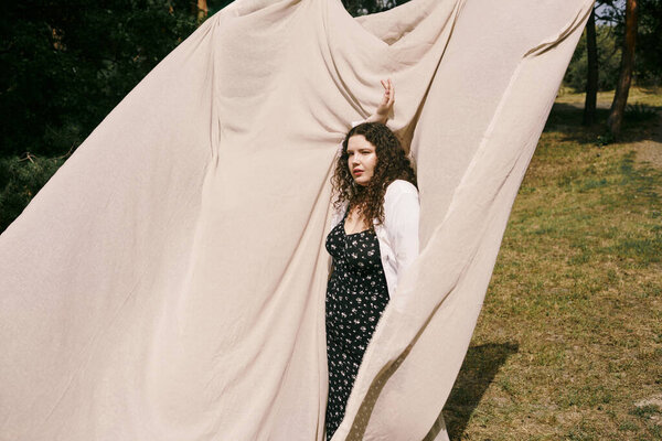 A confident plus size woman stands gracefully in a sunny field, embracing her beauty.