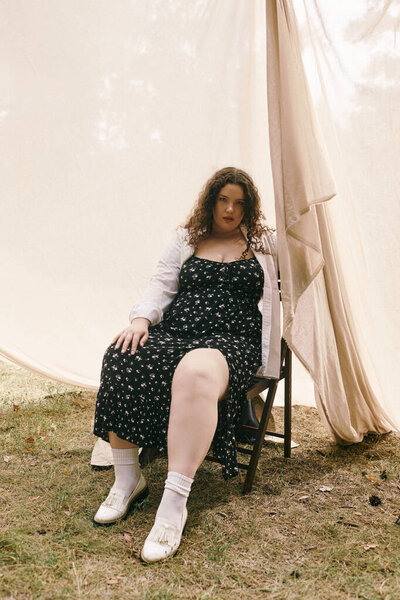 A plus size woman in a floral dress relaxes in a tranquil field under soft sunlight.