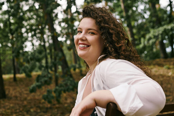 Красивая женщина plus size наслаждается моментом в серенькой дикости и буйных деревьях.