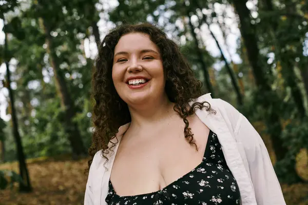 stock image A cheerful plus size woman with curly hair revels in the beauty of nature surrounded by trees.