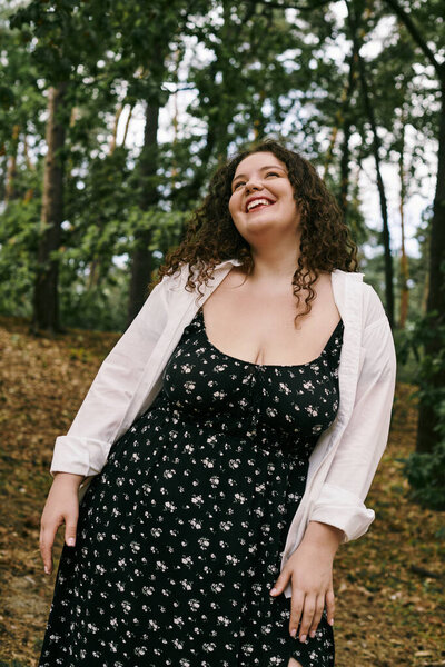 Веселая женщина plus size ярко улыбается в окружении пышной зелени и мягкого солнечного света.