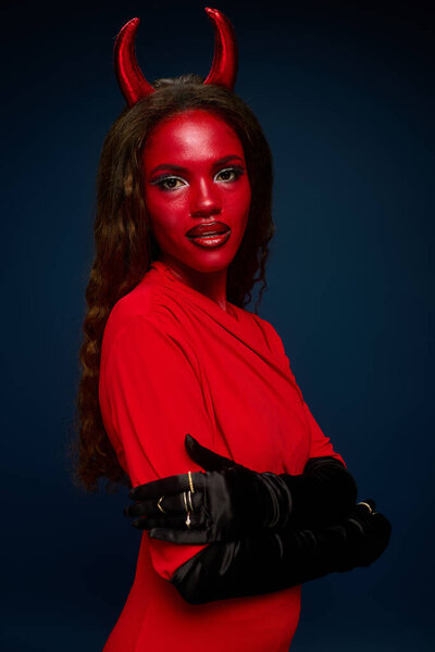 A striking woman dressed as a devil showcases her vivid Halloween look with red skin and horns.