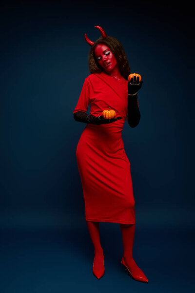 This woman embraces Halloween, wearing a bold costume and playfully interacting with pumpkins.