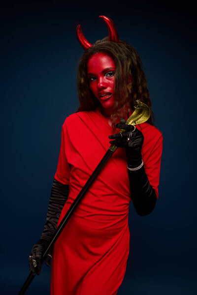 A stunning woman in a red costume poses confidently, embracing her Halloween spirit.