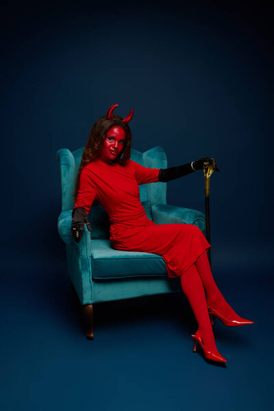 An alluring figure dressed in a striking red costume exudes confidence while seated elegantly.