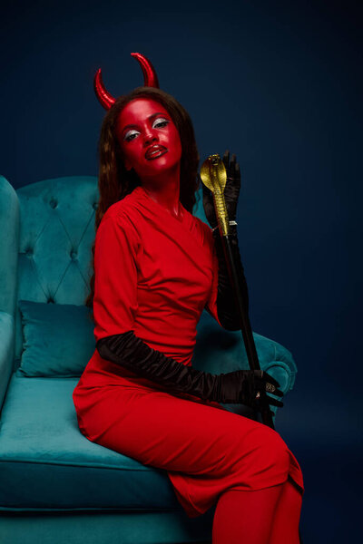 A captivating woman in a bright red Halloween outfit poses confidently with a golden accessory.