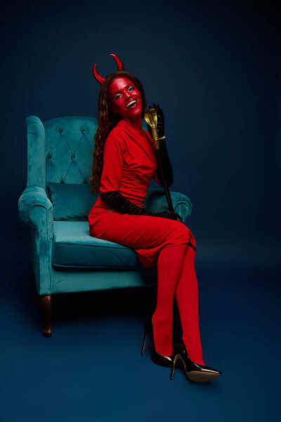 A beautiful woman in a striking red Halloween costume exudes joy while seated gracefully.