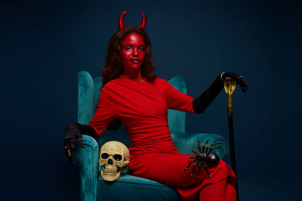 A devilish figure lounges gracefully amidst spooky decorations in a vibrant scene.