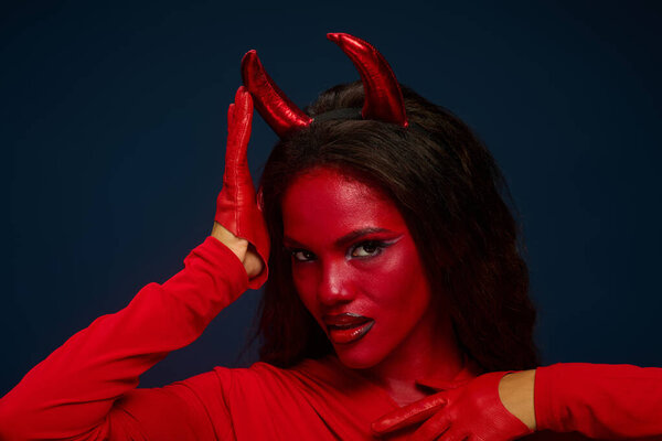 Dressed in vibrant red, a captivating woman playfully poses, embodying Halloween spirit.