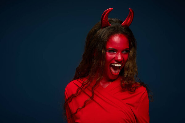 A stunning woman showcases her Halloween spirit with a bold devil costume, exuding energy and joy.