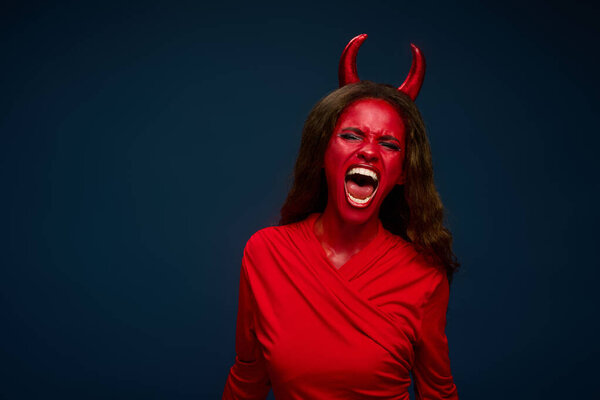 A woman in stunning red attire channels her inner devil, expressing excitement for Halloween.