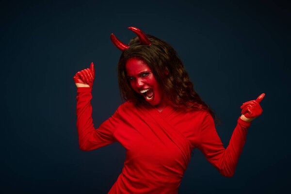 A striking woman dressed in a bold red devil outfit joyfully poses, exuding Halloween spirit.