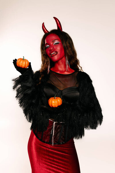 A stunning woman in a dramatic Halloween outfit, playfully showcasing small pumpkins.