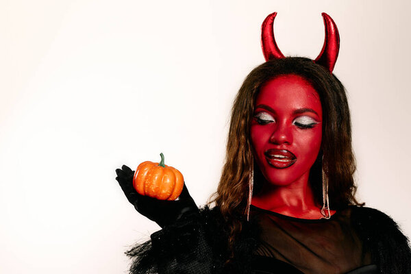 A stunning woman dressed for Halloween displays a mini pumpkin while showcasing her striking look.