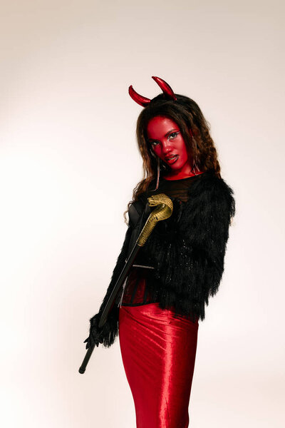 A beautiful woman confidently poses in a striking red devil outfit and makeup.