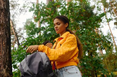 A young woman enjoys the beauty of a colorful autumn forest while adjusting her backpack. clipart