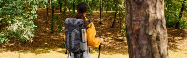 A young woman immerses herself in nature, exploring the colorful fall foliage while hiking. clipart