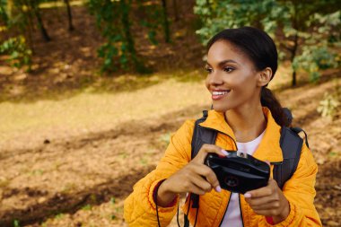 A young woman enjoys hiking through a colorful autumn forest, capturing beautiful memories along the way. clipart