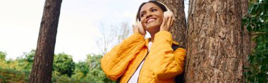 A joyful young woman explores the forest, embracing the autumn colors while enjoying her hike. clipart