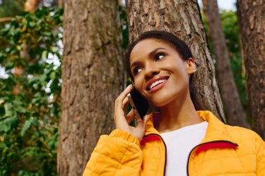 Genç bir Afrikalı Amerikalı kadın, güz yürüyüşü sırasında telefonuyla konuşurken ışıl ışıl gülümsüyor..