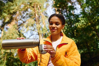 Renkli bir ormanda yürürken, genç bir kadın içkisini termostan dolduruyor, sonbaharın güzelliğini kucaklıyor..