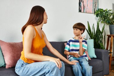 Bir anne, rahat yaşam alanlarında otururken işitme engelli oğluyla sevgiyle meşgul olur..