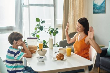 İşitme engelli küçük bir çocuk kahvaltıda annesiyle etkileşime girer ve kahkahalarını paylaşır..