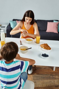 Küçük bir çocuk sıcak bir evde özenli annesiyle kahvaltı ediyor..