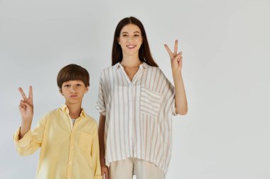 Gülümseyen bir anne ve oğlu parmaklarıyla barış işareti yaparak mutluluklarını ifade ederler..