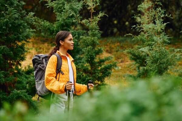 A young African American woman enjoys her hike through a colorful forest, surrounded by autumn foliage.