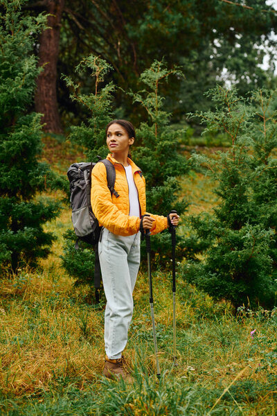 A young African American woman enjoys hiking in a colorful autumn forest, surrounded by lush greenery.
