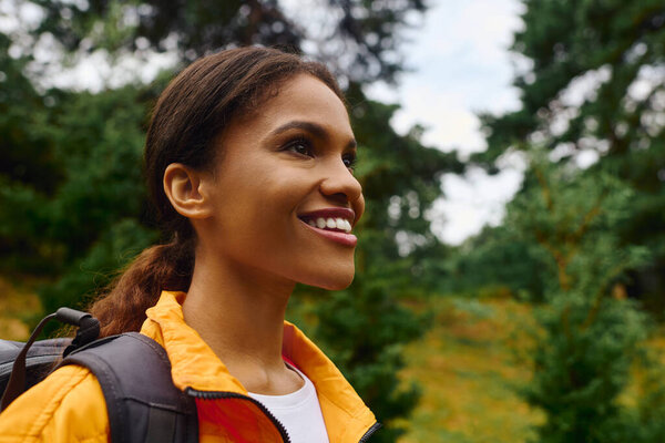 Веселая молодая женщина исследует лесную тропу, восхищаясь осенней листвой и природной красотой.