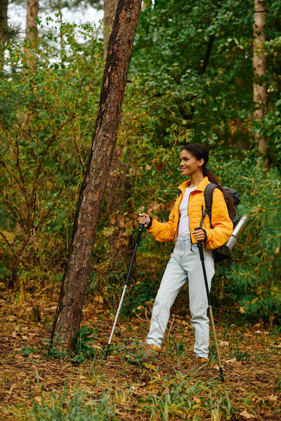 A young African American woman explores a picturesque forest during autumn, embracing nature beauty.