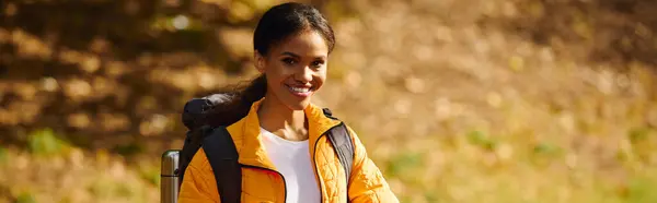 stock image A young African American woman treks through colorful autumn woods, surrounded by fallen leaves and nature.