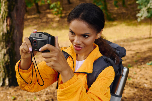 Молодая афроамериканка наслаждается походами по осеннему лесу, запечатлевая прекрасные моменты.
