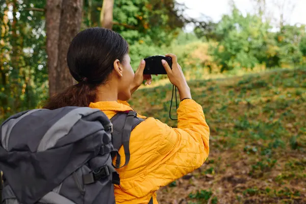 stock image A young African American woman with a backpack takes a moment to capture the autumn colors while hiking.