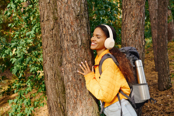 Молодая женщина обнимает дерево, улыбаясь, когда она соединяется с природой во время своего осеннего похода.
