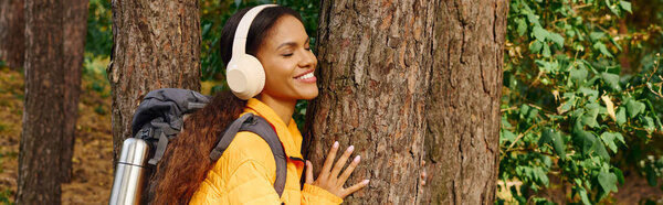 Молодая женщина наслаждается радостным моментом на открытом воздухе, соединяясь с деревом во время похода осенью красочными объятиями.