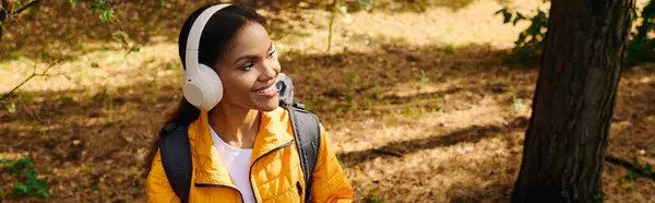 stock image A young African American woman explores a colorful autumn forest, radiating joy and adventure.