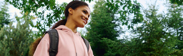 A young African American woman enjoys a refreshing hike through a colorful autumn forest, embracing nature beauty.